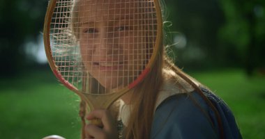 Neşeli kız yaz parkında badminton raketiyle komik suratlar yapıyor..