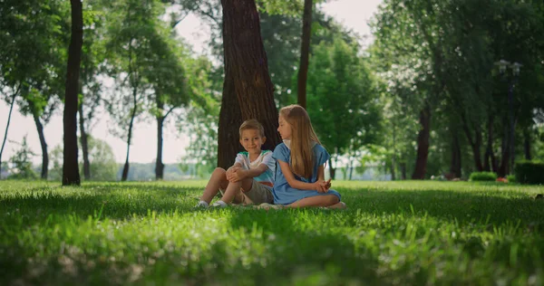 Счастливые дети сидят рядом с деревом на зеленой траве. Милая девочка-мальчик играет на природе. — стоковое фото