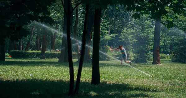 Verspielter kleiner Junge, der im grünen Park Wasser sprüht und Ohren vor Spritzwasser versteckt — Stockfoto