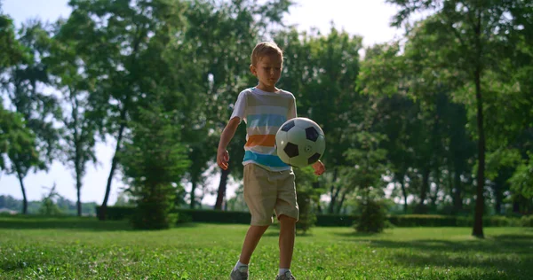 Rapaz desportivo faz exercício de futebol no parque. Jovem atleta chutar bola no gramado ensolarado — Fotografia de Stock