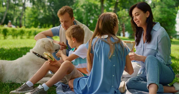 小さな男の子はピクニックでラブラドールを養う。緑の芝生の上で陽気な家族の休息. — ストック写真