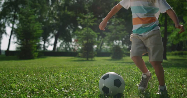 Rapaz feliz joga futebol à luz do sol no parque. Criança faz exercício de futebol na natureza. — Fotografia de Stock