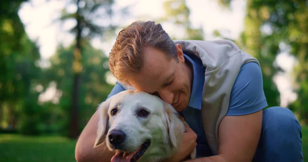 Lächelnder Mann mit Leine im Park. Besitzer kuscheln Augen zu und kuscheln lieblichen Hund — Stockfoto