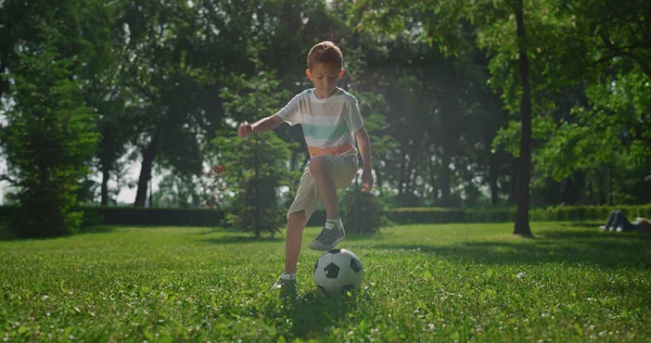 Jovem fazendo exercício de futebol na grama no parque. Criança jogar futebol ao ar livre. — Fotografia de Stock