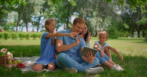 Leende familj viftande händer kommunicera med hjälp av tablett på naturen på sommardagen. — Stockfoto