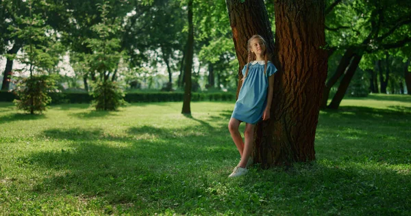 Chica soñadora magra tronco del árbol en el parque. Sonriente niño observando la naturaleza alrededor —  Fotos de Stock