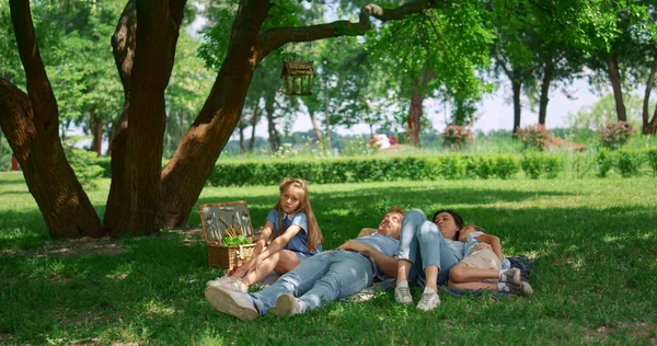 Familia relajada acostada sobre hierba verde en el picnic. La gente tranquila descansa en el parque. — Foto de Stock