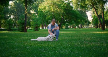 Güler yüzlü av köpeği sahibi çömelmiş bir vaziyette oturur. Odaklanmış köpek yalan söylüyor..