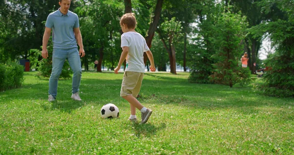 Homem desportivo passando bola para filho ativo no parque verde. Pai jogar futebol com menino — Fotografia de Stock