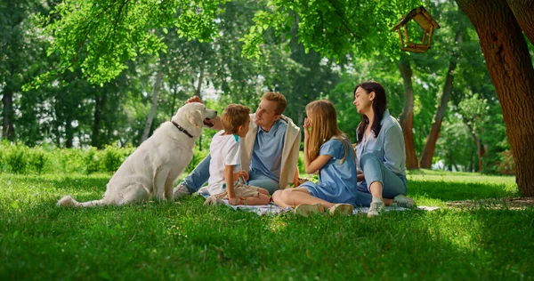 Jovem família carícia labrador em piquenique. Pessoas felizes descansam com o cão lá fora. — Fotografia de Stock