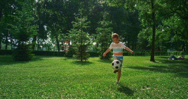 Kleiner Junge kickt Fußball. Konzentriertes Kind übt allein im Sommerpark. — Stockfoto