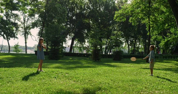 Pari sisarusta pelaa sulkapallomailoja vihreällä puistolla. Kesäpiknik — kuvapankkivalokuva