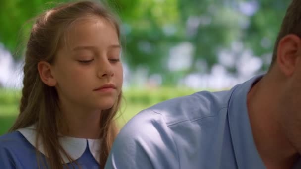 Girl sitting near father on lawn close up. Child watching tablet in father hands — Stock Video