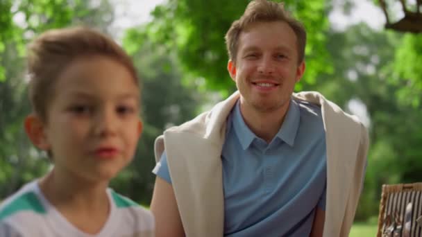 Augenzwinkernder glücklicher Mann, der in Großaufnahme in die Kamera lacht. Vater sitzt mit Sohn auf Picknick. — Stockvideo
