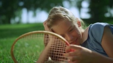 Gülümseyen kız yeşil çimlerde tek başına yatıyor. Sarışın çocuk raketi yakından dokundu.