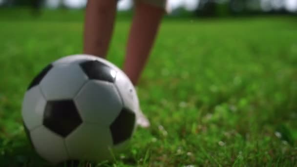 サッカーボールを蹴る子供の足を閉じます。少年は公園の緑の芝生で遊ぶ. — ストック動画