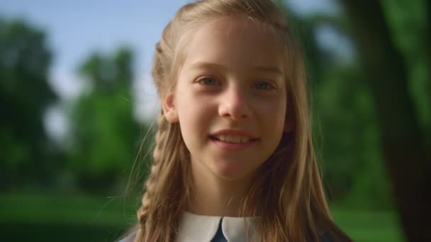 Chica rubia posando sola con trenza de cerca. Niño suave mira la cámara en el parque — Vídeos de Stock