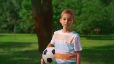 Futbol topuyla doğaya poz veren bir çocuk. Ciddi küçük atlet yakın plan.