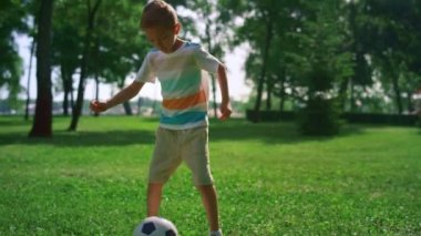 Küçük çocuk futbol maçından önce antrenman yapıyor. Çocuk güneşli parkta tek başına ısınıyor..