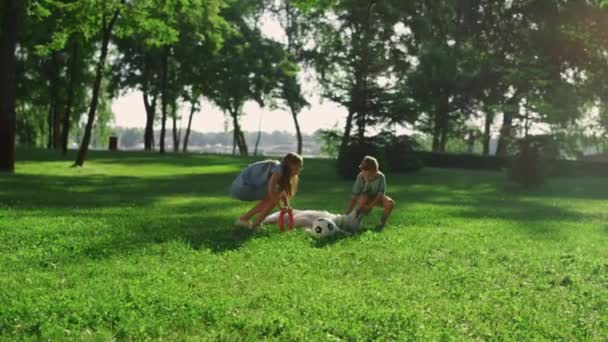 Glada syskon klappa golden retriever i parken. Hund liggande på grönt fält. — Stockvideo