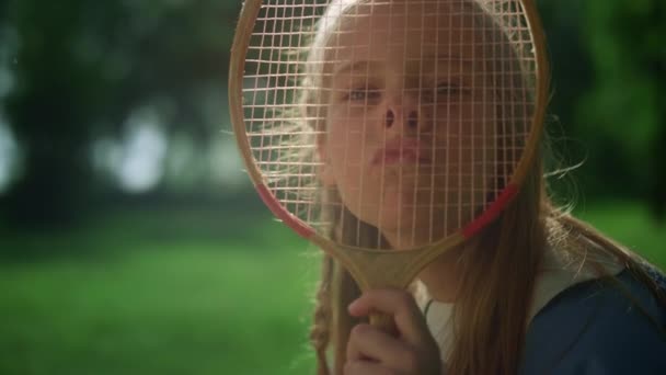 Glædelig pige gør sjove ansigter med badminton ketcher i sommerparken closeup. – Stock-video