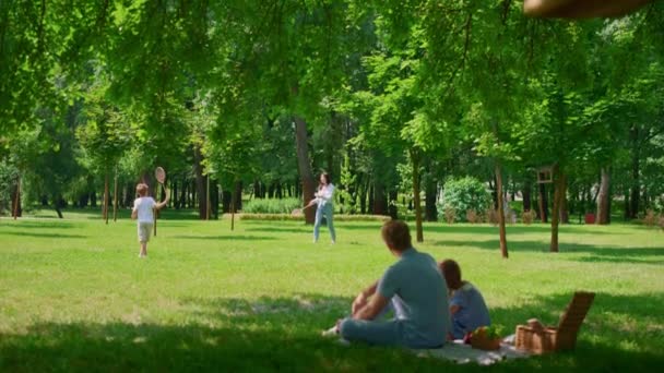 Vader kijkt badminton wedstrijd met gaughter op de picknick. Actieve gezinsrust. — Stockvideo