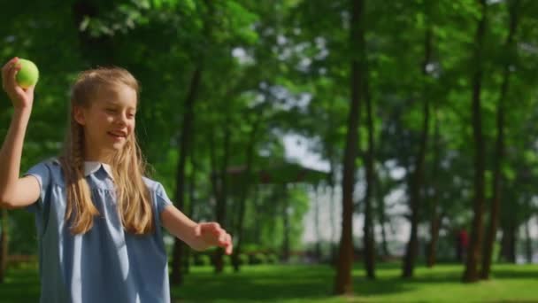 Lächelnde Mädchen werfen Ball auf der grünen Wiese Nahaufnahme. Glückliches Kind spielt Fang im Park. — Stockvideo