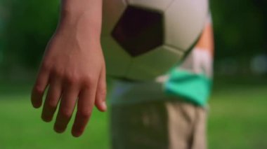 Kimliği belirsiz çocuk elinde soccerball topunu tutuyor. Çocuk kolu topu çayırda tutuyor.