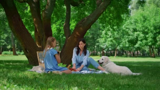 Feliz madre descansando con su hija en el picnic. Familia con perro relajarse al aire libre. — Vídeo de stock