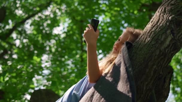 Dívka ležící s telefonem na větvi zblízka. Usmívající se dítě sledující smartphone. — Stock video