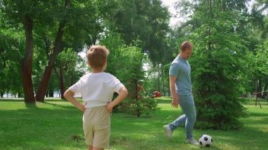 Baba oğluyla yeşil çimlerde futbol oynuyor. Baba oğlanla oyun oynamayı seviyor..