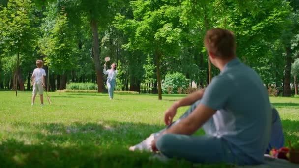 Jovem pai assistindo jogo badminton visão turva. Atividade no ar fresco no parque — Vídeo de Stock