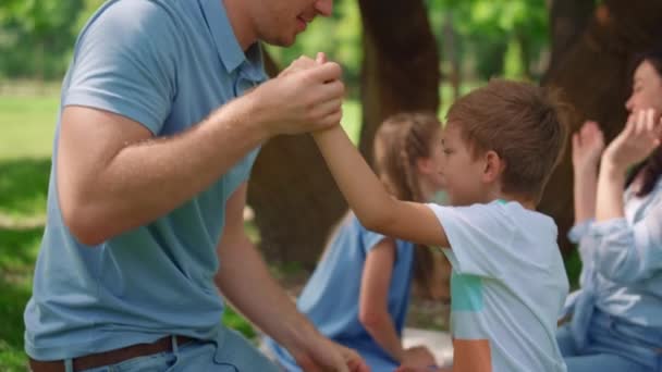 Vater mittleren Alters kitzelt Sohn auf Picknick-Nahaufnahme. Aktive Familien spielen lustige Spiele — Stockvideo