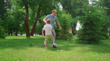 Mutlu baba oğluna futbol öğretiyor. Neşeli çocuk çimlerde babama pas atıyor..