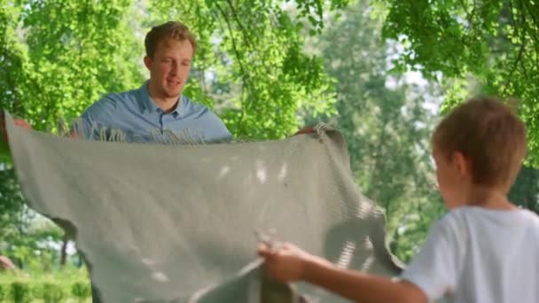 O pequeno filho ajuda o pai a espalhar cobertor. Mentira familiar despreocupada no ar fresco. — Vídeo de Stock