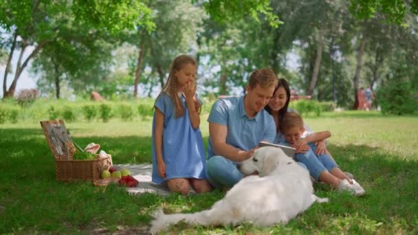 Glad familj använda tablett på picknick. Föräldrar tittar på laptop med två barn utanför — Stockvideo