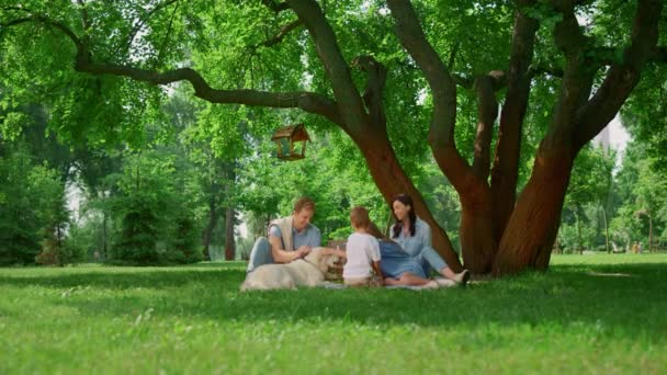 Ruhige Familie mit Hund beim Picknick. Glückliche Menschen entspannen auf grünem Gras im Freien — Stockvideo