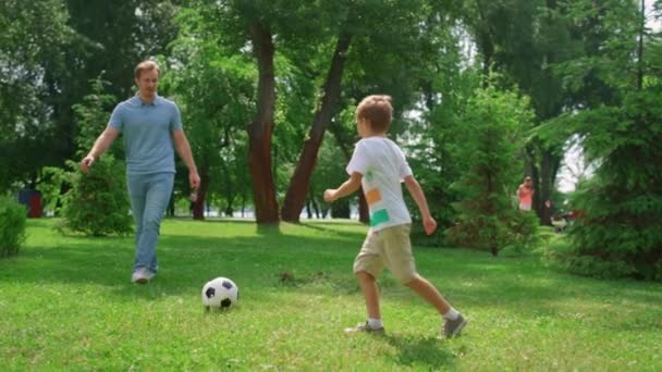 Homem desportivo passando bola para filho ativo no parque verde. Pai jogar futebol com menino — Vídeo de Stock