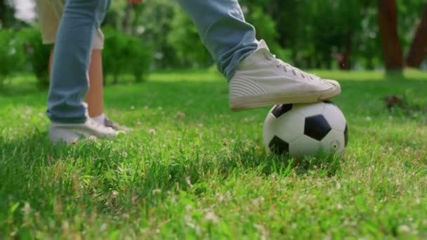 Ismeretlen emberi lábak rúgják a labdát a fűben közelről. Apa focizik a fiával.. — Stock videók