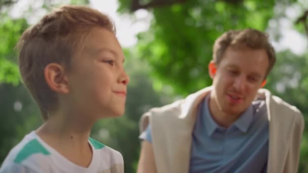 Ein lachender Junge im Gespräch mit seinem Vater beim Picknick. Familienessen im Park. — Stockvideo