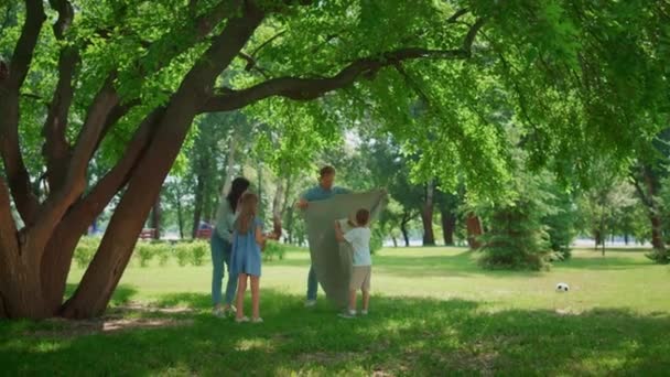 Junge Familien picknicken auf Rasenrasen. Eltern bereiten Mittagessen mit zwei Kindern zu. — Stockvideo