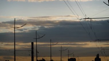 Gri kabarık bulutlar gün batımında şehrin üzerinde hareket ediyor. Elektrik kabloları fenerleri..