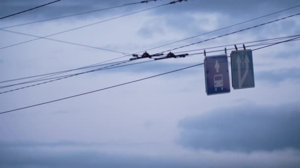 Mavi yol işaretleri bulutlu gökyüzünde sallanıyor. Yakın çekim tramvayı trafiği hızlandırıyor — Stok video
