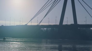 Modern şehir köprüsü akşam güneşini aydınlatıyor. Su yüzeyi yolu yansıtıyor.
