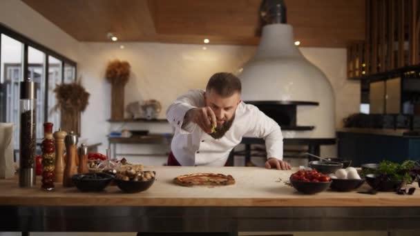 Muž vaří pizzu v italské restauraci. Šéfkuchař přidává ingredience na pečivo. — Stock video