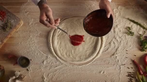 Chef spreading tomato sauce on pizza. Baker man hands cooking food in kitchen. — Stock Video