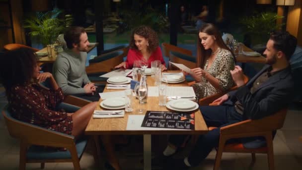 Различные друзья разговаривают друг с другом на причудливой встрече в ресторане на уютном вечере. — стоковое видео
