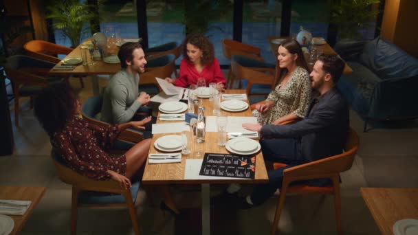 Wieloetniczna grupa przyjaciół świętuje zabawę w eleganckiej restauracji wieczorem. — Wideo stockowe