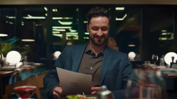 Lächelnder Mann beim Blick auf Speisekarte im Restaurant. Kerl sitzt an schickem Esstisch.