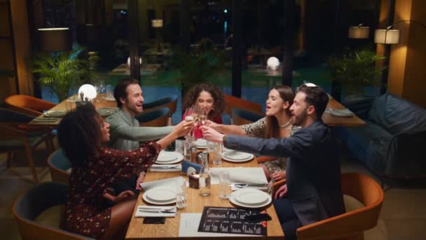 Amigos felices festejando bebiendo en el restaurante. La gente multiétnica hace tostadas. — Vídeo de stock